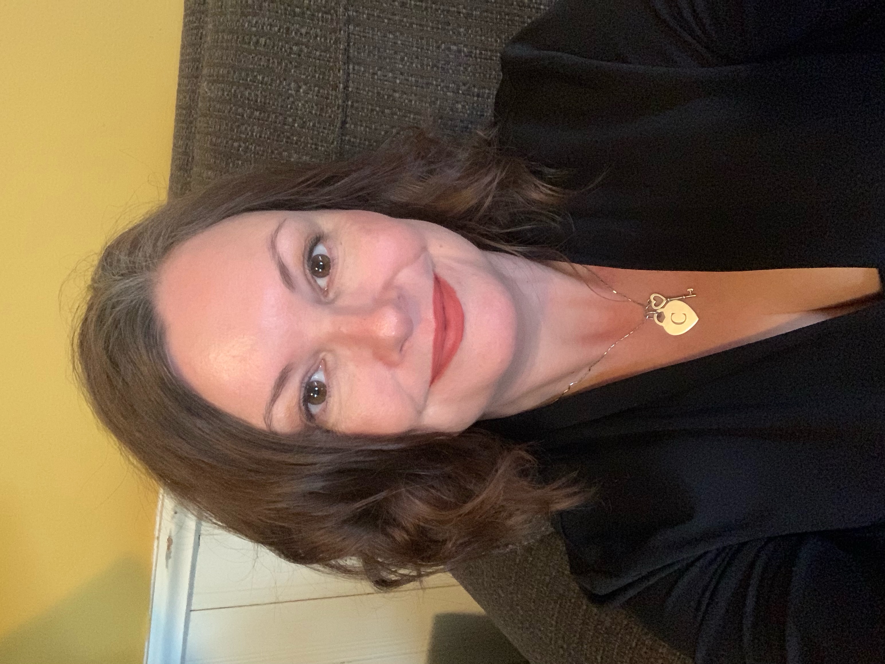 A self portrait of Connie Spencer, a woman with brunette hair. In this photo, she wears a black blouse and gold necklace.